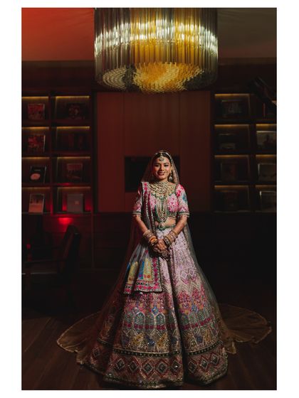 A stunning portrait of the bride in her intricately designed lehenga, standing under a grand chandelier.
