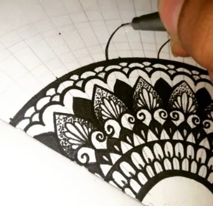 My hand at work, filling in the patterns of a semi-mandala. You can see the underlying grid I use to guide the drawing. This step-by-step process is what makes creating complex designs manageable for beginners.
