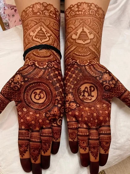 The start of a beautiful stain on this personalized engagement mehendi, with the initials and rings clearly visible.