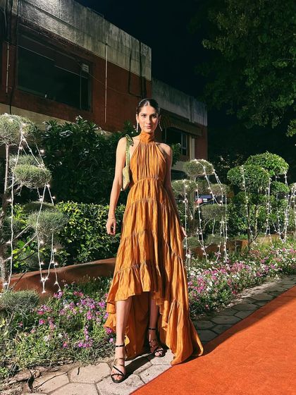 An elegant evening look featuring a tiered, high-low mustard dress with a beautiful halter neck tie.