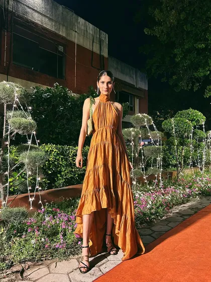 An elegant evening look featuring a tiered, high-low mustard dress with a beautiful halter neck tie.