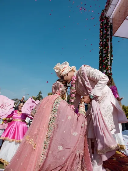 The perfect exchange. A beautiful shot of the Varmala ceremony, with dancers holding large floral props in the background, adding to the festive decor.