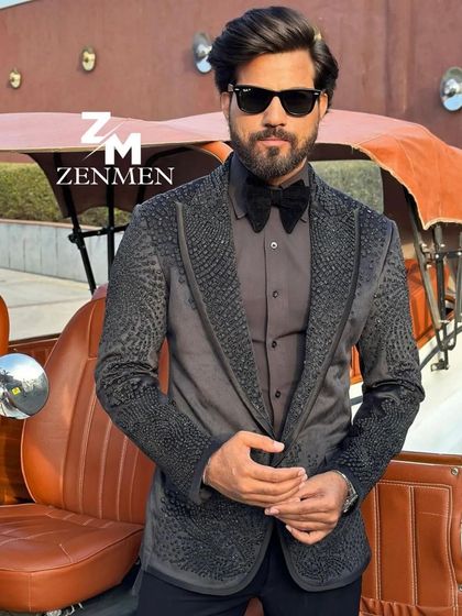 A model looking dapper in a grey tuxedo with all-over black crystal embellishments. The vintage car in the background adds to the classic, sophisticated vibe.
