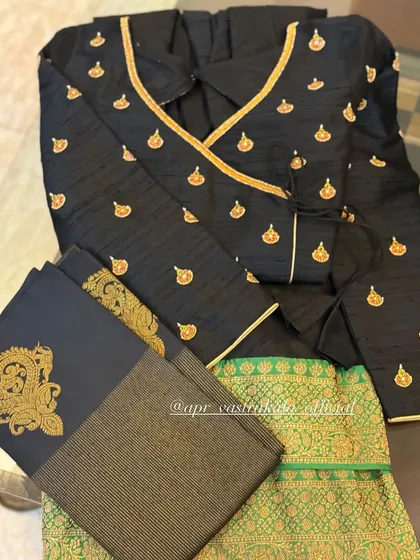 A stylish angrakha-style wrap blouse in black, featuring gold butti embroidery and piping. It is paired with a green brocade skirt for a chic, modern ethnic look.