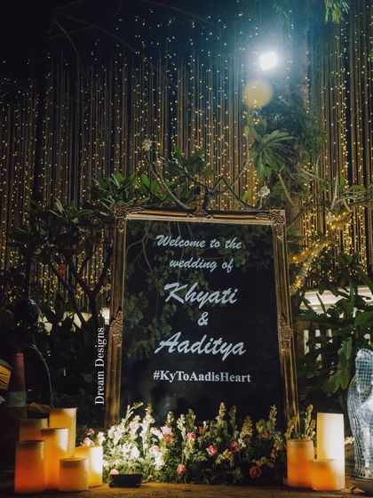 A personalized welcome sign is a beautiful touch. This one, set in an ornate golden frame and surrounded by candles, greets guests against a backdrop of fairy lights.