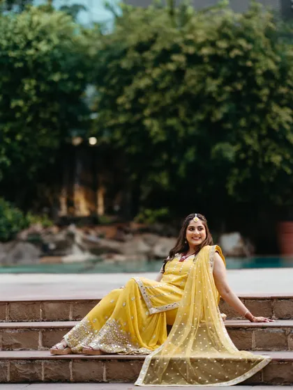 A relaxed and happy portrait of the bride during her mehndi ceremony. Seated on the steps, her yellow outfit glows, and her smile is infectious.