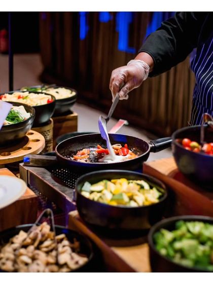 A chef prepares a pasta dish with a colourful array of fresh, prepped vegetables ready to be added. This emphasizes our use of fresh ingredients and the made to order nature of our live pasta bar.