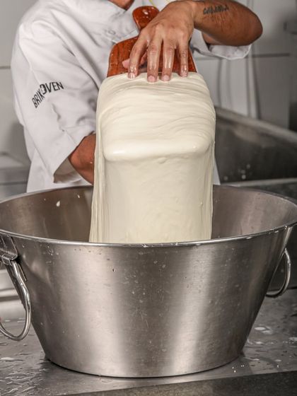 A large mass of fresh mozzarella being stretched in a stainless steel bowl, showcasing the scale of our in-house cheese production.