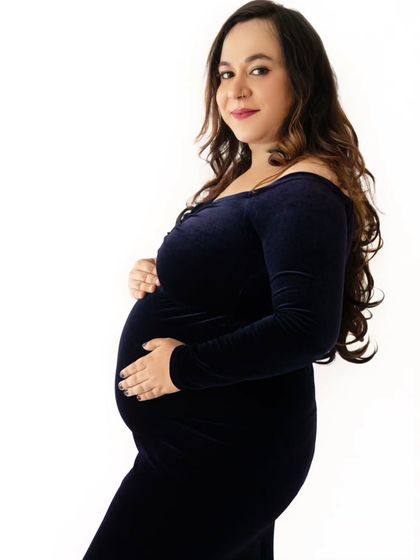 A simple and elegant profile shot of a mom-to-be in a form-fitting blue velvet gown against a clean white background.