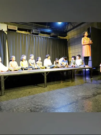 A group of our youngest performers sitting on the edge of the stage, completely engaged in their instructor's lesson.