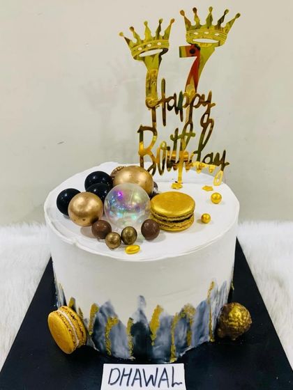 A modern and masculine cake for a 17th birthday. The design features a black, white, and gold color scheme with a marble effect, macarons, and crown toppers.
