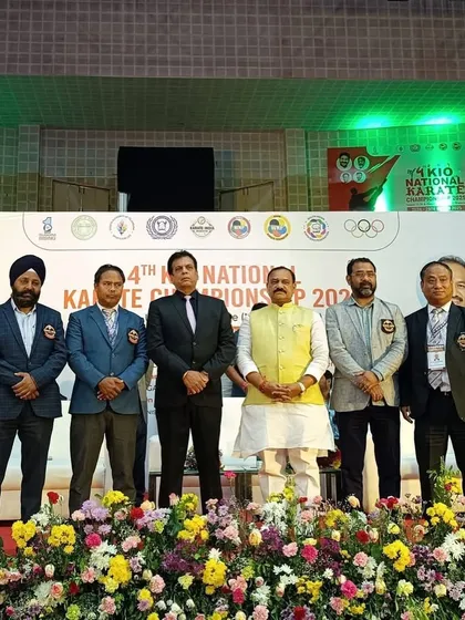 Standing with dignitaries and officials on the main stage of the 4th KIO National Championship in Hyderabad. The presence of government officials underscores the event's national importance.