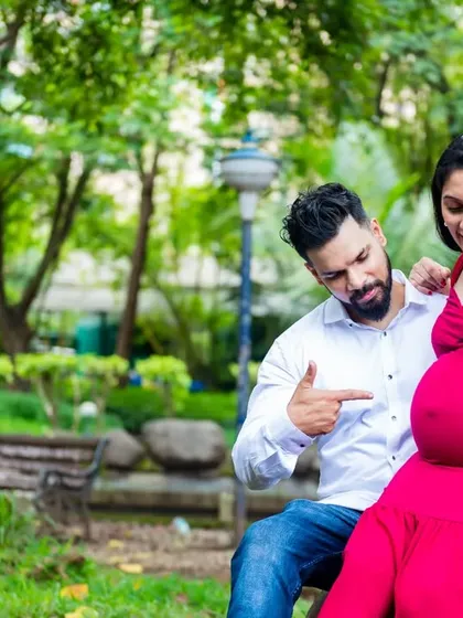 A fun, candid moment in the park. The couple playfully points to the baby bump, the center of their world.