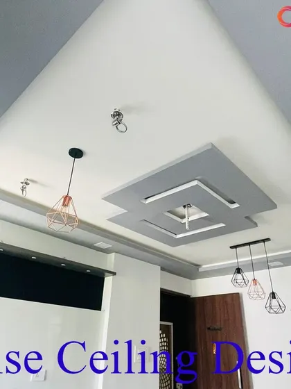 A contemporary living room ceiling with a layered, offset square design in grey and white. The structure is prepared for the installation of multiple pendant lights and includes integrated speakers for a complete media experience.