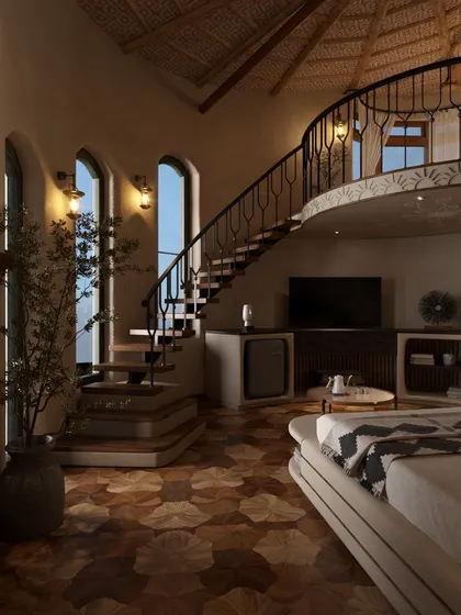The same duplex suite viewed in the soft, warm light of the evening. The interior lighting highlights the beautiful grain of the wooden floors and the elegant curve of the wrought-iron staircase railing.