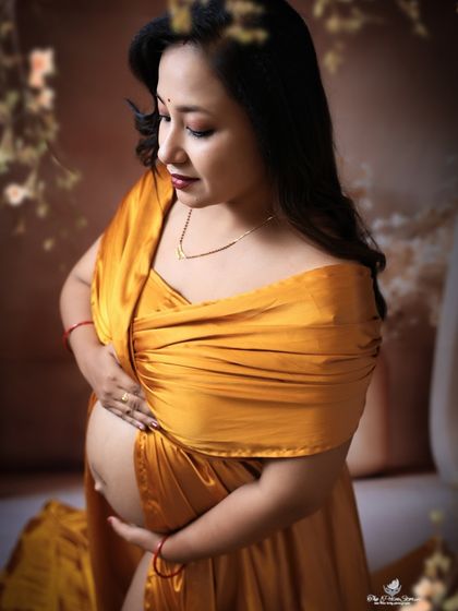 A beautiful close-up focusing on the mom-to-be's glowing face and her hands cradling the baby bump. The rich yellow satin fabric adds a touch of luxury.