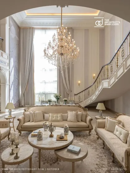 The grand staircase of The Ivory Royale sweeps past the formal living area, its elegant curve complementing the classic lines of the furniture. The double-height windows flood the space with natural light, highlighting the luxurious textures and finishes.