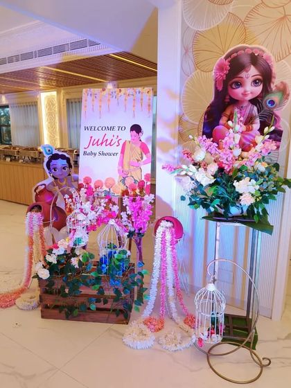 An entrance decoration for a Krishna-themed baby shower. We used a welcome standee, character cutouts, and floral arrangements with decorative birdcages to greet the guests.