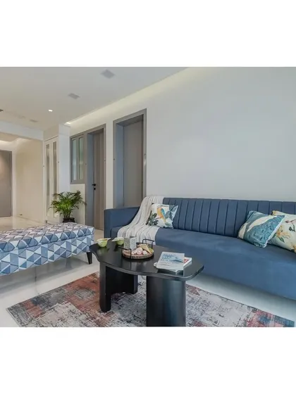 Comfort is key in any living room design. This view showcases the plush, channel-tufted blue sofa, paired with a geometric-print ottoman and a modern black coffee table. It’s a practical and stylish setup for everyday living.