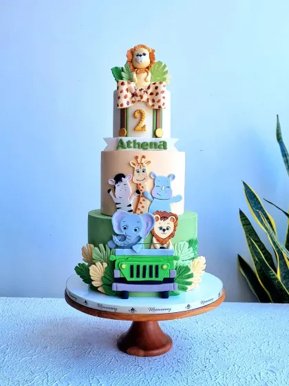 A grand three-tier safari adventure cake, perfect for a milestone birthday. This design features a whole crew of friendly, handmade fondant animals like a lion, elephant, and giraffe in a jeep, set against a backdrop of fondant leaves, creating a fun jungle expedition theme.