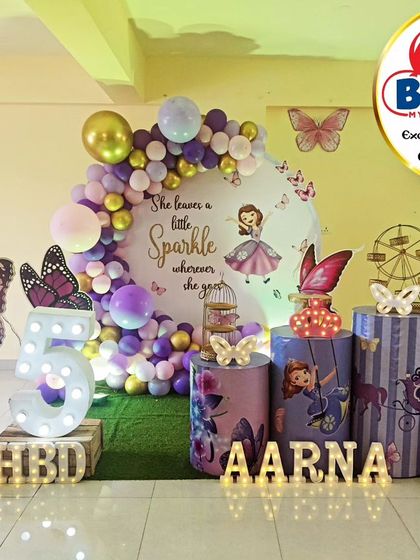 A magical Sofia the First-themed fifth birthday. The purple and pink decor features a 'She leaves a little sparkle' backdrop, character cutouts, and a large light-up number '5'.