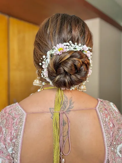 A detailed shot of the bridal bun, beautifully decorated with a wreath of fresh baby's breath and pink daisies.