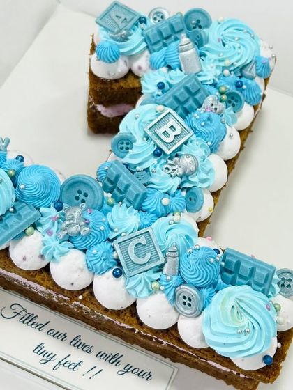 A beautiful number '1' monogram cake for a baby girl's first birthday. The blue theme is accented with edible baby blocks, buttons, and chocolate bars.