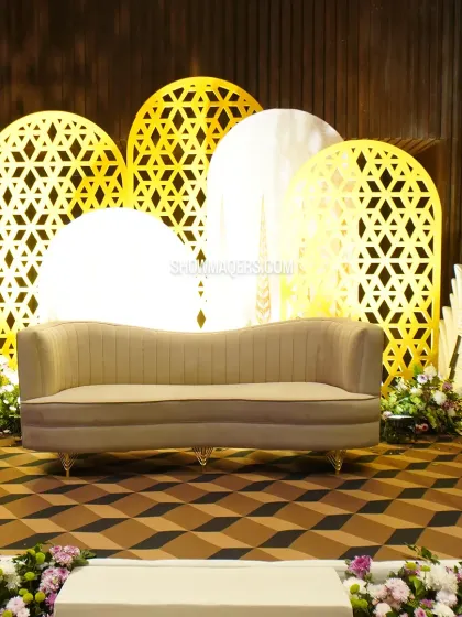 A modern stage for the couple, featuring backlit jaali panels in abstract shapes and a clean, contemporary sofa.