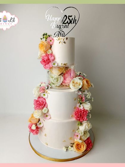 A stunning floral cake for a 25th anniversary. This tiered design features a separator and a cascade of beautiful fresh flowers in shades of pink and peach.