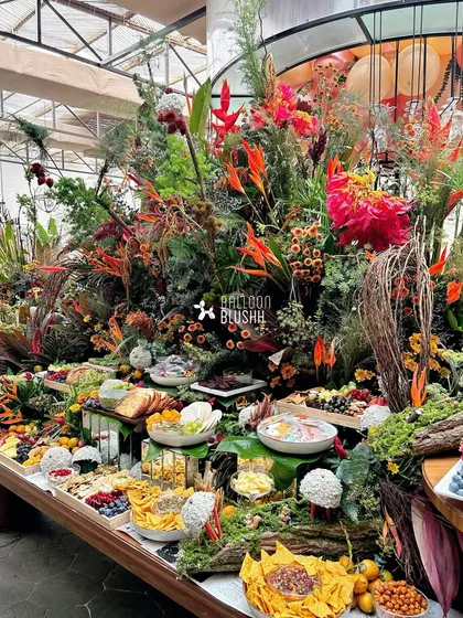 An elaborate grazing table designed for a woodland-themed baby shower. The food is seamlessly integrated into a landscape of moss, ferns, and vibrant wildflowers, turning the culinary experience into a work of art.