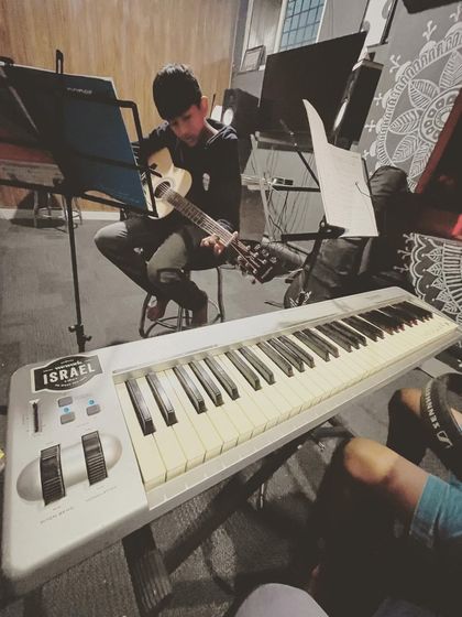 A young student practices his ukulele, with a keyboard in the foreground, showcasing the variety of instruments available to learn at our school.