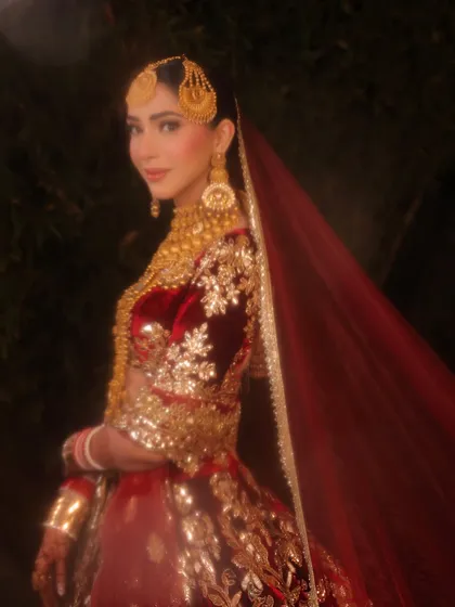 A dreamy, soft-focus shot of the bride in her magnificent red and gold reception lehenga. The makeup is kept warm and glowing to match the romantic mood.