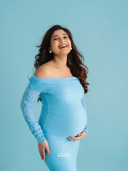 A happy, candid-style portrait of a mother-to-be in a light blue gown.