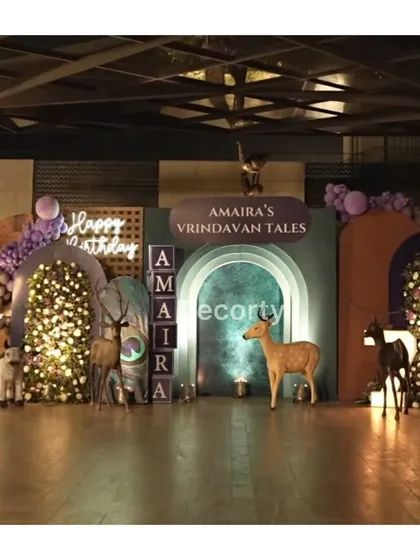 A grand stage setup for 'Amaira's Vrindavan Tales', a Krishna-themed celebration. The decor features multiple backdrops, floral walls, animal props, and custom light-up name blocks for a truly magical atmosphere.