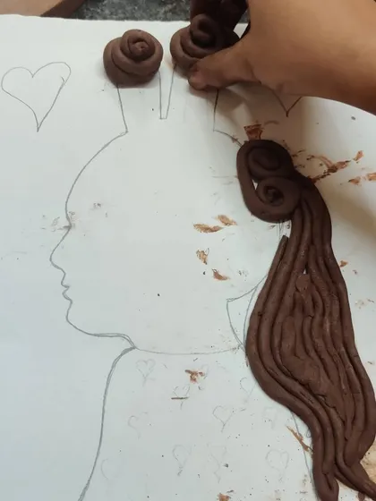 A hand places rolled clay coils onto a pencil drawn silhouette of a princess. This shows the process of our clay enhanced silhouette projects, where drawing and sculpting come together.