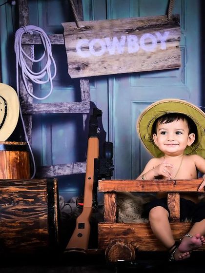 A charming little cowboy sitting in a rustic wooden cart, looking ready for the wild west.