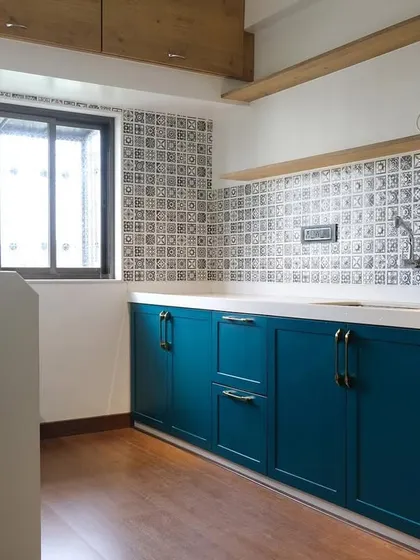 A wider shot of the PU finish kitchen, showing the complete layout with its wooden flooring, patterned backsplash, and dual-tone cabinetry, creating a warm and inviting space.