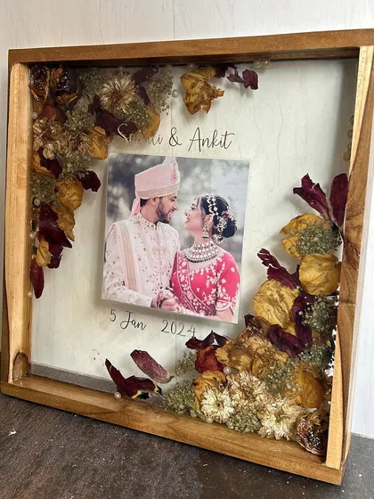 A close-up of another varmala preservation frame, showing the intricate arrangement of dried flowers and the couple's photo.