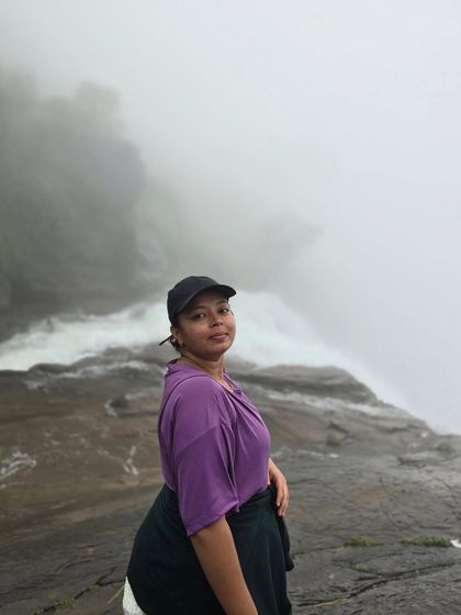 A trekker poses at the edge of Bandaje Falls, with the mist creating a dramatic backdrop.