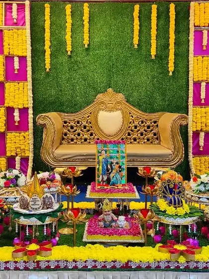 A colorful baby shower setup with a vibrant checkered backdrop in yellow, pink, and green. The plate decoration includes traditionally dressed dolls and a variety of offerings.