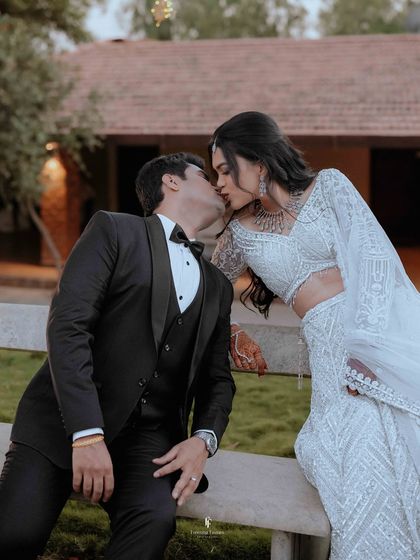 A romantic kiss shared by the couple at their outdoor reception. The natural setting and their elegant attire create a beautiful contrast.