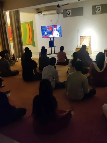 The Sangha sits in meditation, absorbing the energies of the rituals. The space becomes a vessel for both the Guru's stillness and Devi's vibrancy.