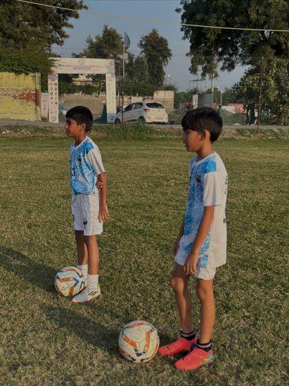 Our shining stars learning the fundamentals. Two of our youngest players stand ready with their footballs, eager to begin their training drills.