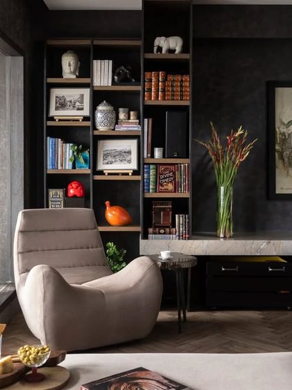 A close-up of a reading corner in the Caitriona apartment. The 'Botero Chair' offers a comfortable spot to relax, surrounded by a curated collection of books, art, and personal objects that make the space feel truly lived-in.