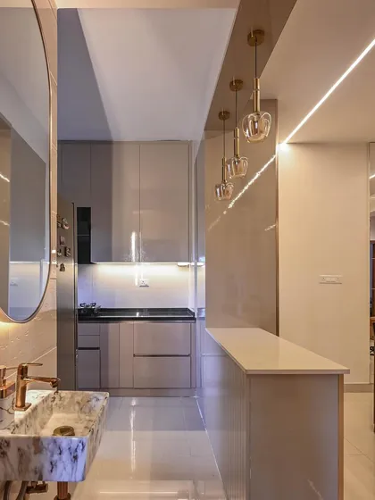 This view shows the open-plan kitchen and wash basin area in the Aarohi Residence. We used a neutral color palette with high-gloss cabinets, a striking marble basin, and elegant pendant lights to create a space that is both highly functional and visually refined.