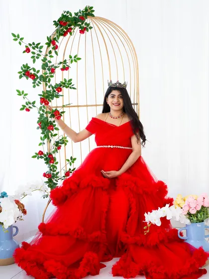 A matching moment of magic. This mother wears a stunning red gown that matches a tiny version for her future baby, posed next to our golden birdcage prop for a whimsical touch.