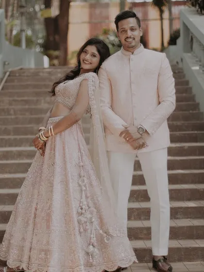 A classic, smiling portrait of the couple posing on a staircase, dressed in sophisticated pastel-colored traditional outfits.