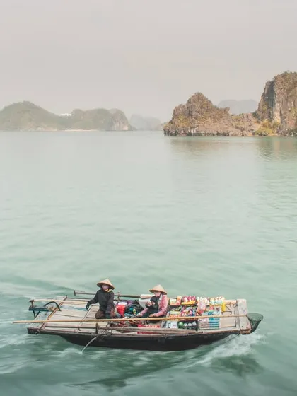 A floating shop boat is dwarfed by the majestic limestone karsts of Halong Bay in the background.