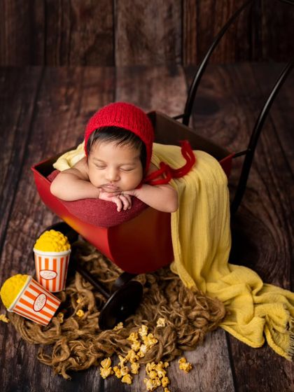 A wider view of the popcorn-themed session. The dark wood background and scattered popcorn create a charming, rustic cinema feel for this unique newborn photo.