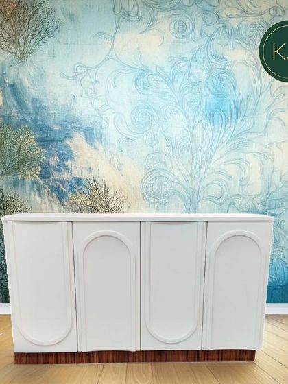 This white cabinet with arched door details and a contrasting wood base is a versatile storage piece. Its clean, modern design can complement a variety of interior styles.